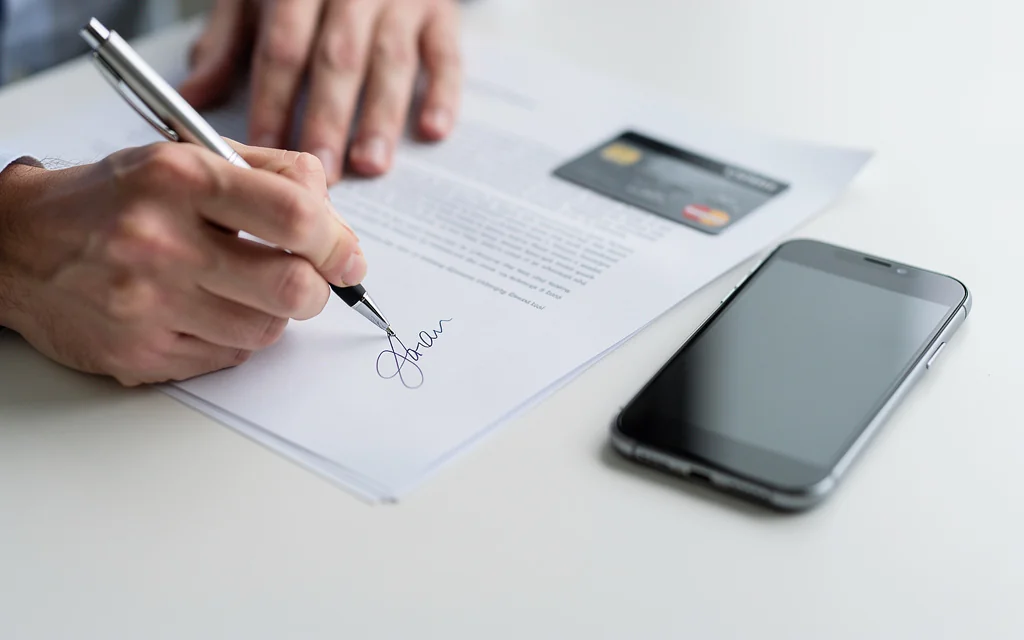 Personne signant des documents d'ouverture de compte bancaire avec une carte et un smartphone